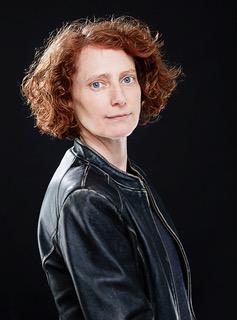 A photo of a woman with light skin and red curly hair wearing a black leather jacket.