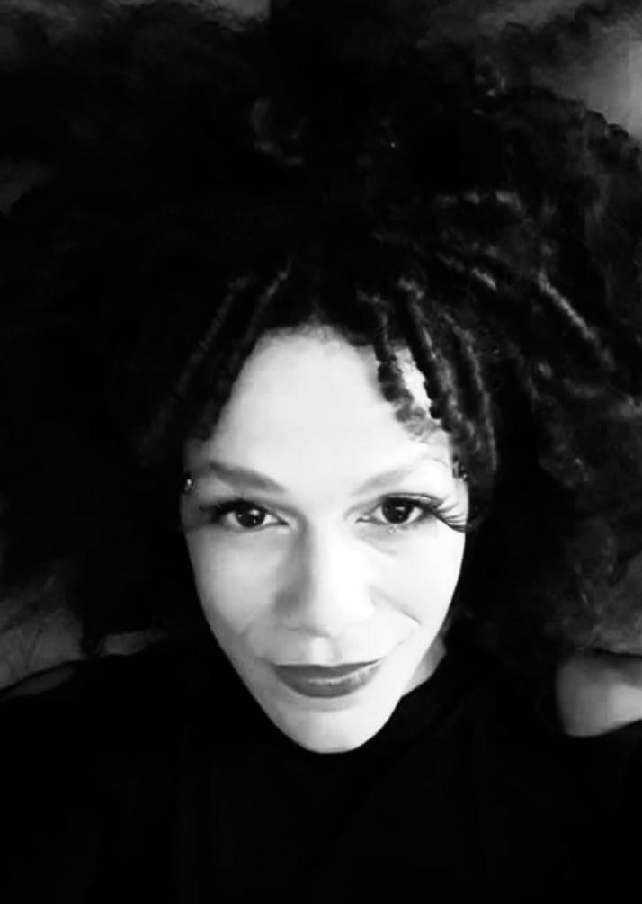 A black and white photo of a woman with dark lipstick and textured curly hair.