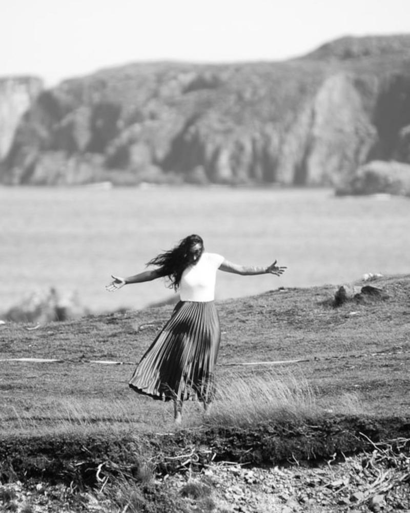 A woman dances on a cliff by the ocean.