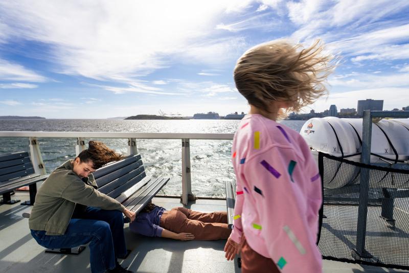Three dancers take positions on a ferry in a bay.