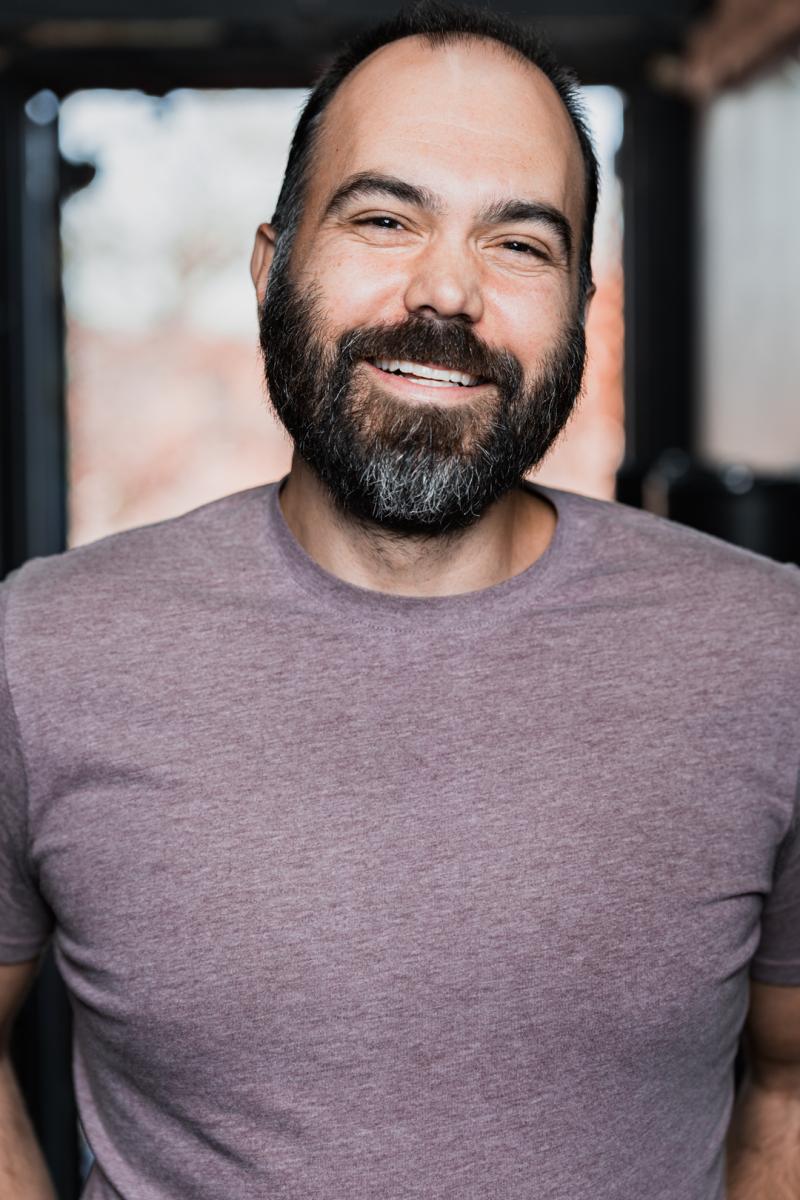 A man with short dark hair and a short beard smiles at the camera.