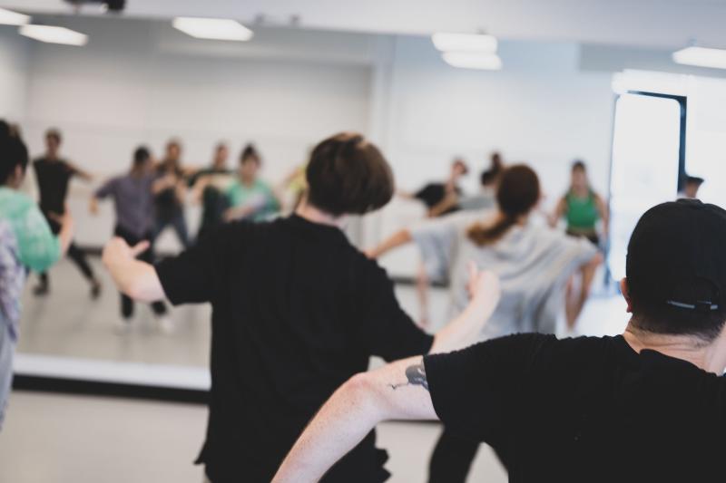 A group of people dance in a studio in front of a mirror.