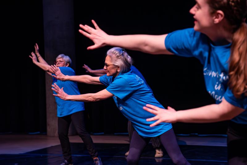 Three people in blue t-shirts reach with joy and energy to the right side edge of the photograph
