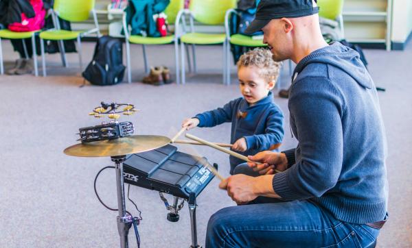 Drummer playing at live at the library with small child watching