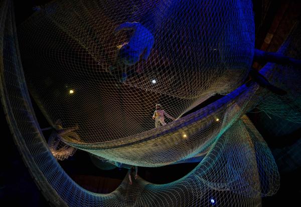 Layers of nets suspended within a large room, under blue and green lighting.