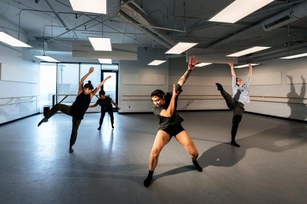 An image of four dancers caught mid movement in a wide bright room.