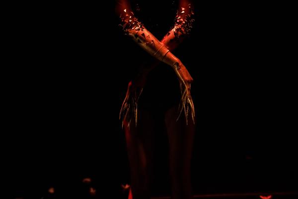 A dancer crosses their forearms in front of their waist, letting their golden gloved hands hang down.