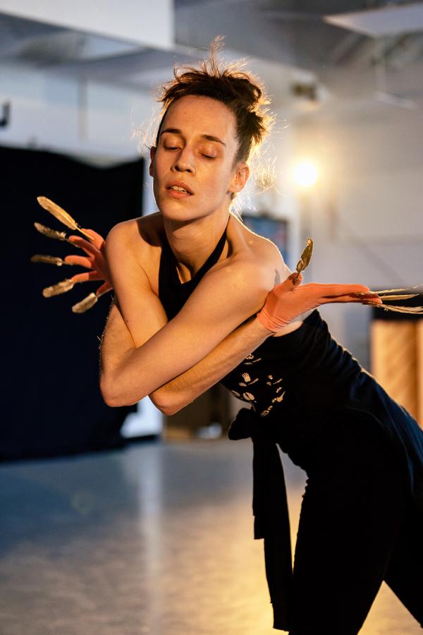 A dancer leans forwards wrapping their extended fingers around their shoulders.