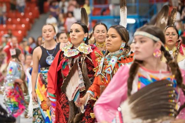 A line of women in colourful regalia line up at a powwow