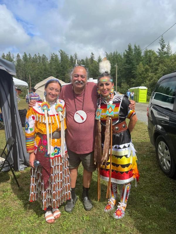 Three people in colourful regalia stand together smiling