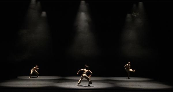 Three people spread out dancing under spotlights on a black stage