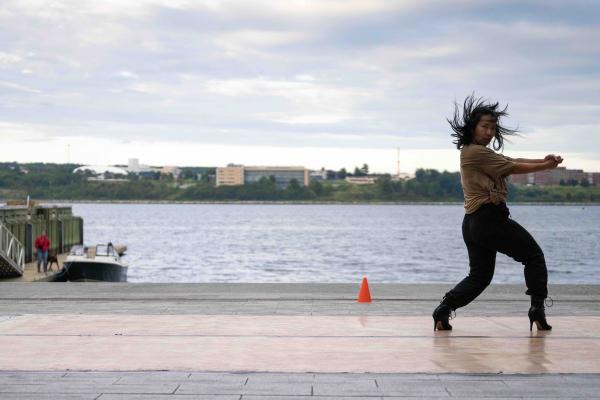 A woman dances in heels in front of a harbour