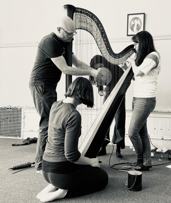 Four people gather around a large harp.