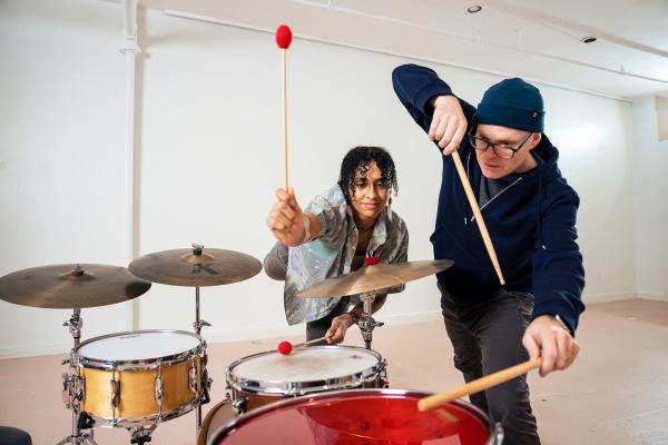 Two people play a drumset together.