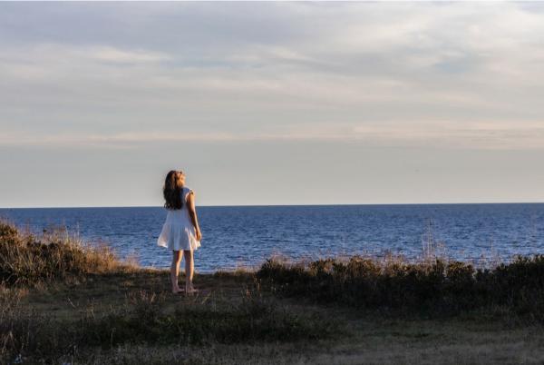 A woman stands on a cliff next to the ocean.