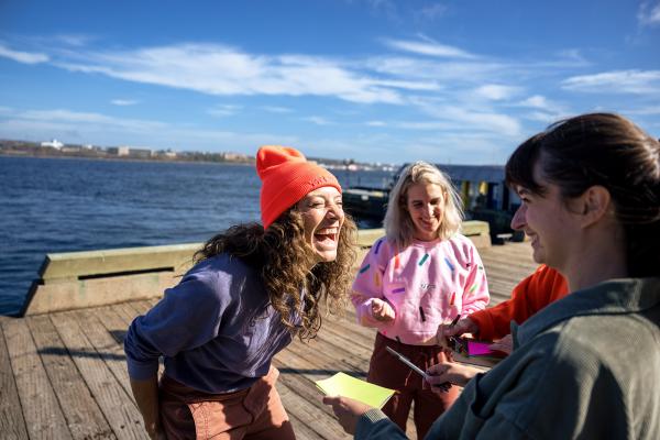 Three people gather on a wooden pier, smiling joyfully.