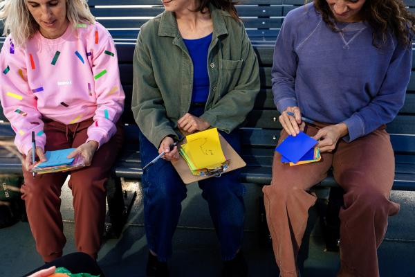 Three people sit on a bench holding colourful post-it notes in their laps.
