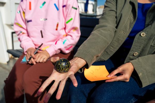 Two people sit on a bench, one holding a patterned ball in her hand.