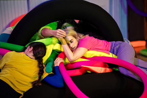 Four people lay on a pile of soft colourful objects.