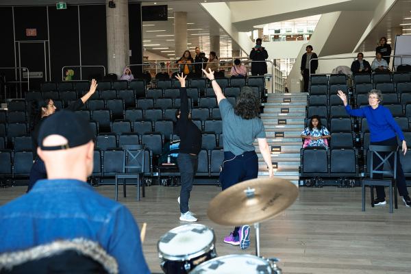 A group of people dance in front of rows of risers.