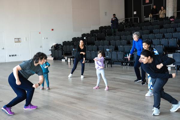 A group of people dance in front of rows of risers.