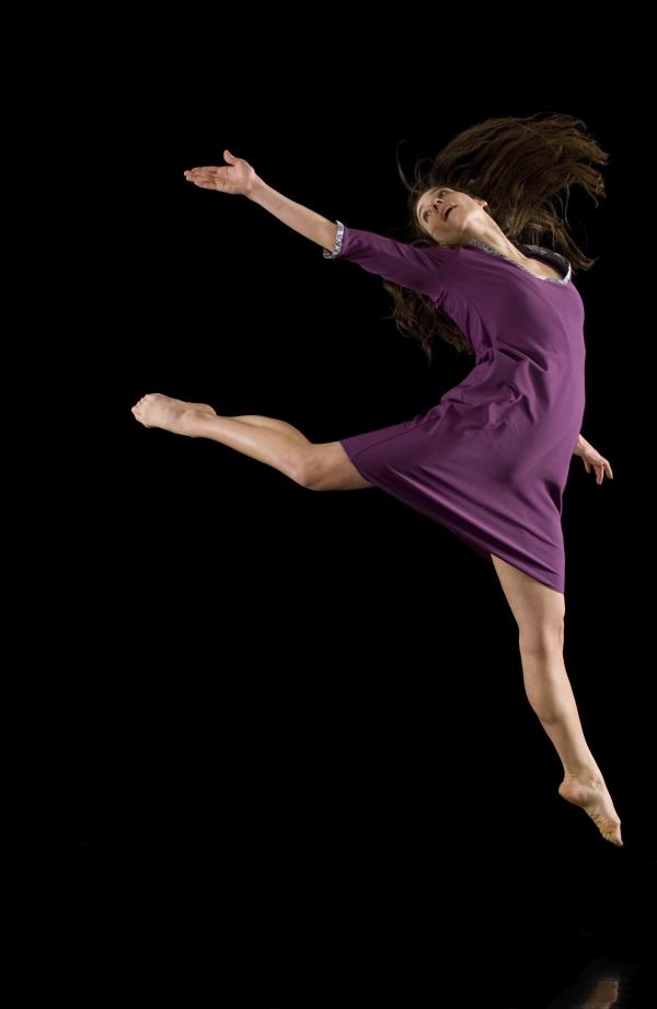 A dancer jumps with her arm extended behind her. 