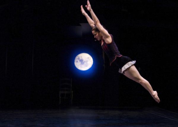 A dancer jumps in front of a backdrop of the night sky and moon.