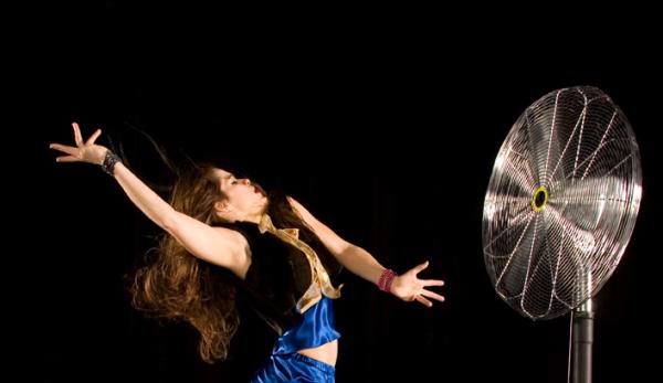 A dancer reaches in front of an electric fan.