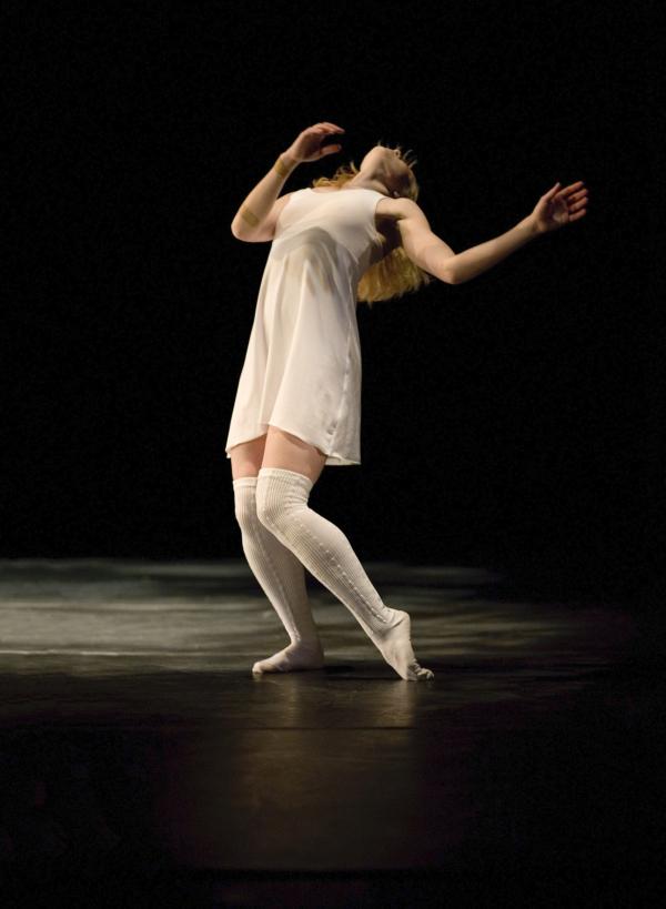 A dancer in a white dress lifts her chest toward the ceiling.