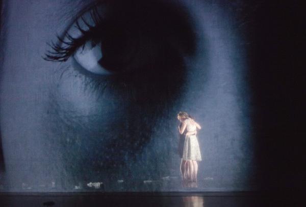 Two dancers hug on stage in front of a photo projection. 