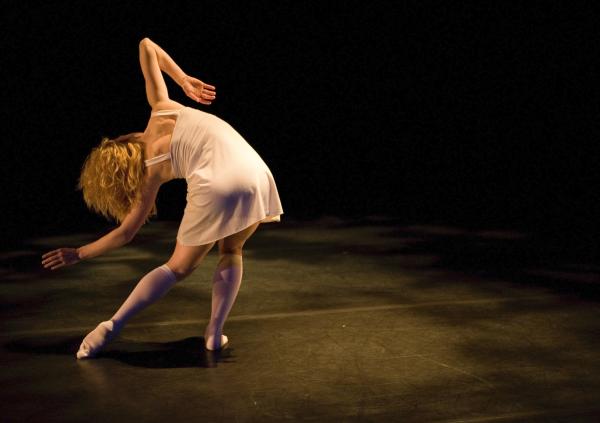 A dancer in a white dress bends sideways, facing the back.