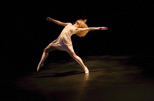 A dancer in a white dress reaches back. 