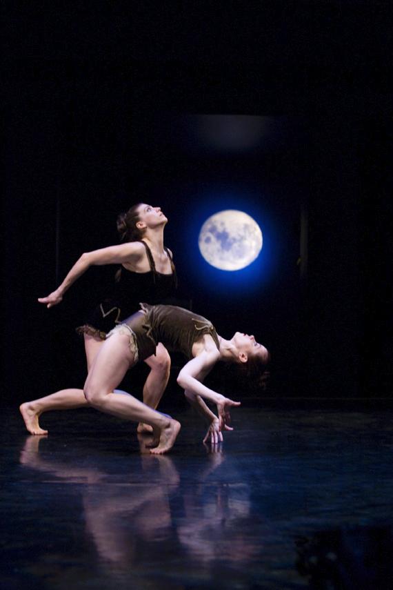 A dancer looks up and another dancer bends backward below her. 