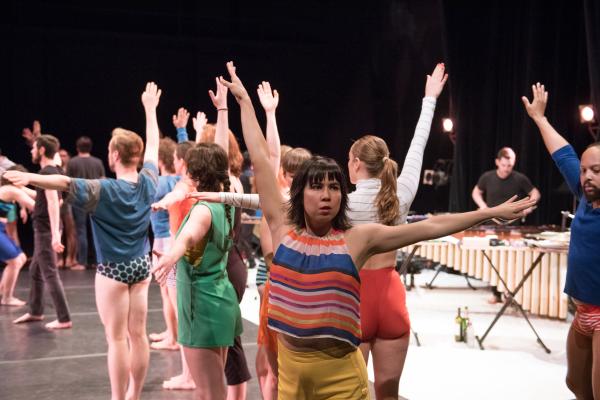 A group of dancers in colourful clothes lift their arms.