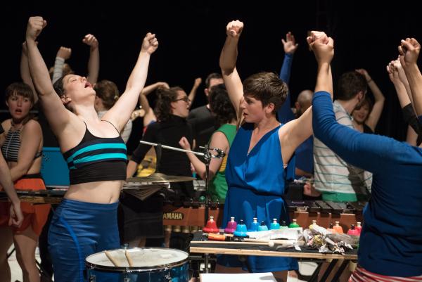 A group of dancers in colourful clothes lift their fists overhead