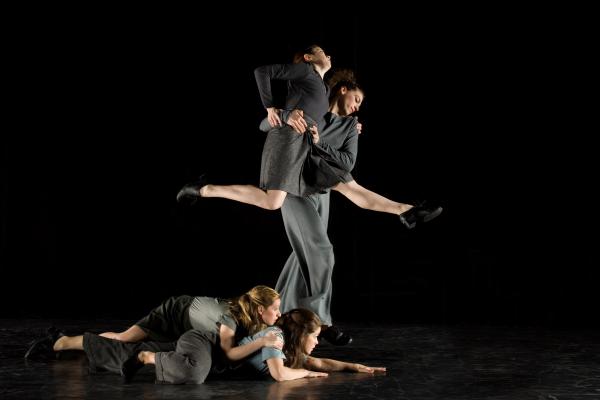 Two dancers lay on the floor below two dancers in a partnering lift.