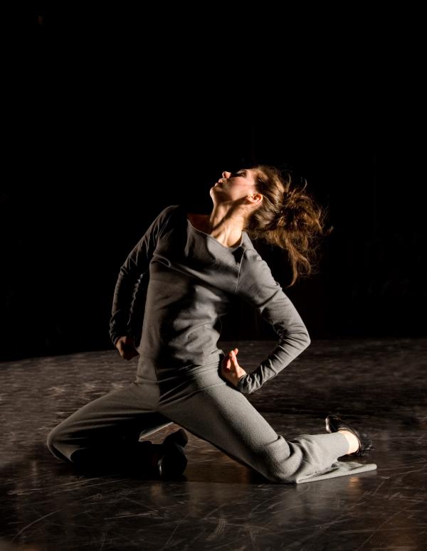 A dancer lunges on the floor with hands on her hips. 