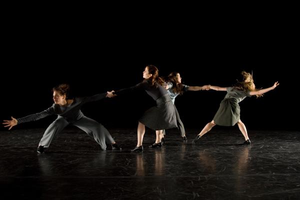 Four dancers hold each other's arms in a line. 