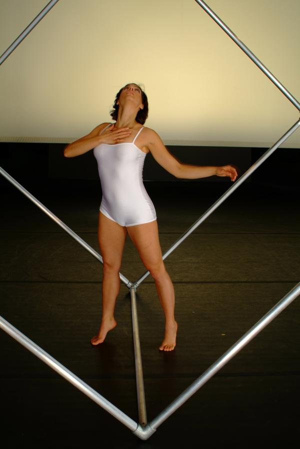 A dancer moves inside a metal cube structure. 