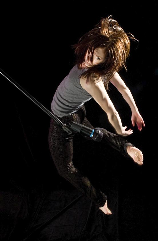 A dancer jumps beside a microphone stand. 