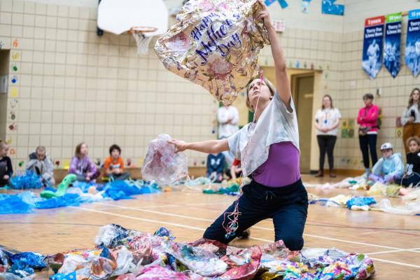 A woman kneels in a pile of plastic garbage, lifting an empty balloon.