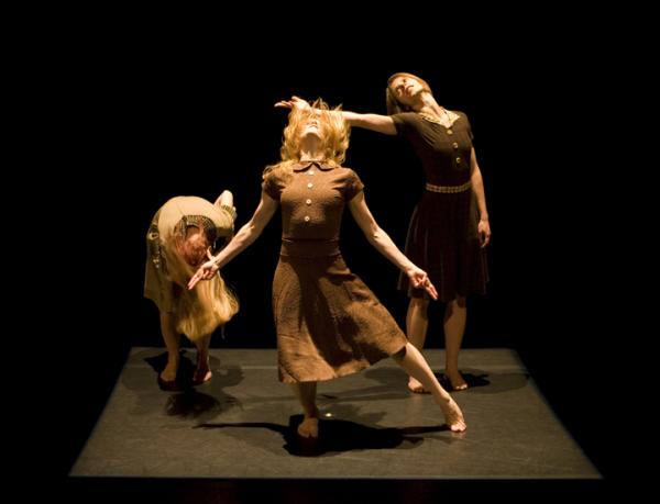 Three dancers in brown dresses are in motion. 