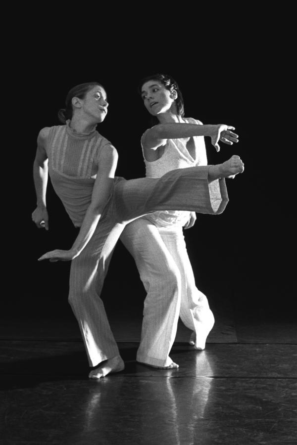 Two dancers in white costumes look at each other in motion. 