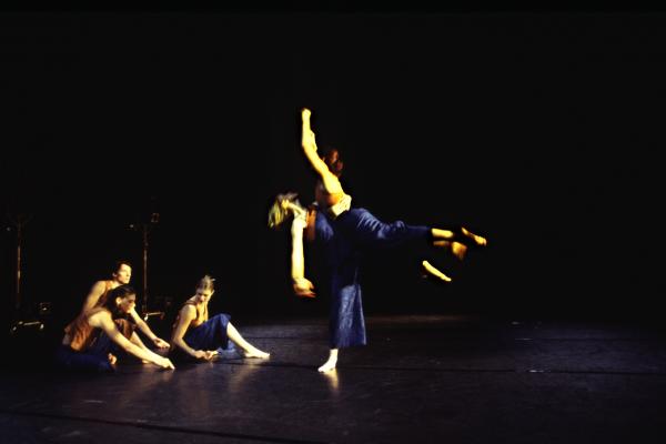 Three dancers sit on the floor as another dancer is lifted into the air. 