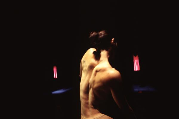 A dancer's bare back is seen in front of a black backdrop. 