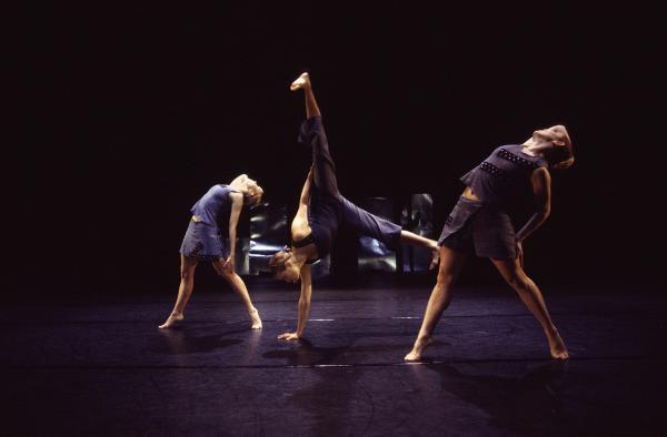 Two dancers look up and another dancer balances on one arm. 