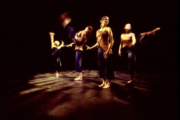 Five dancers move in front of a black backdrop. 