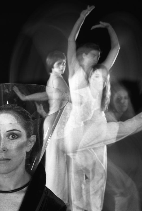 A dancer looks toward the camera as three dancers move behind her. 