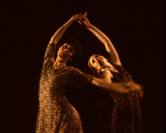 Two dancers spin each other with arms over head. 