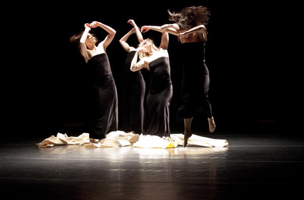 Three dancers stand on piece of canvas, while another jumps in front of them.